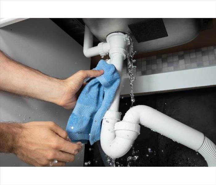 Two hands of someone holding a pipe that is leaking with a blue towel